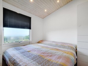 A bedroom with a large window, a bed with a colorful quilt, and a sloped ceiling with recessed lighting.