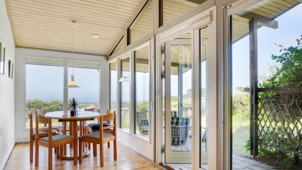 A modern interior with a wooden floor, a round dining table with chairs, and large sliding glass doors leading to an outdoor area with a view of greenery. - "Miona" - 725m from the sea by Interhome (Kalundborg)