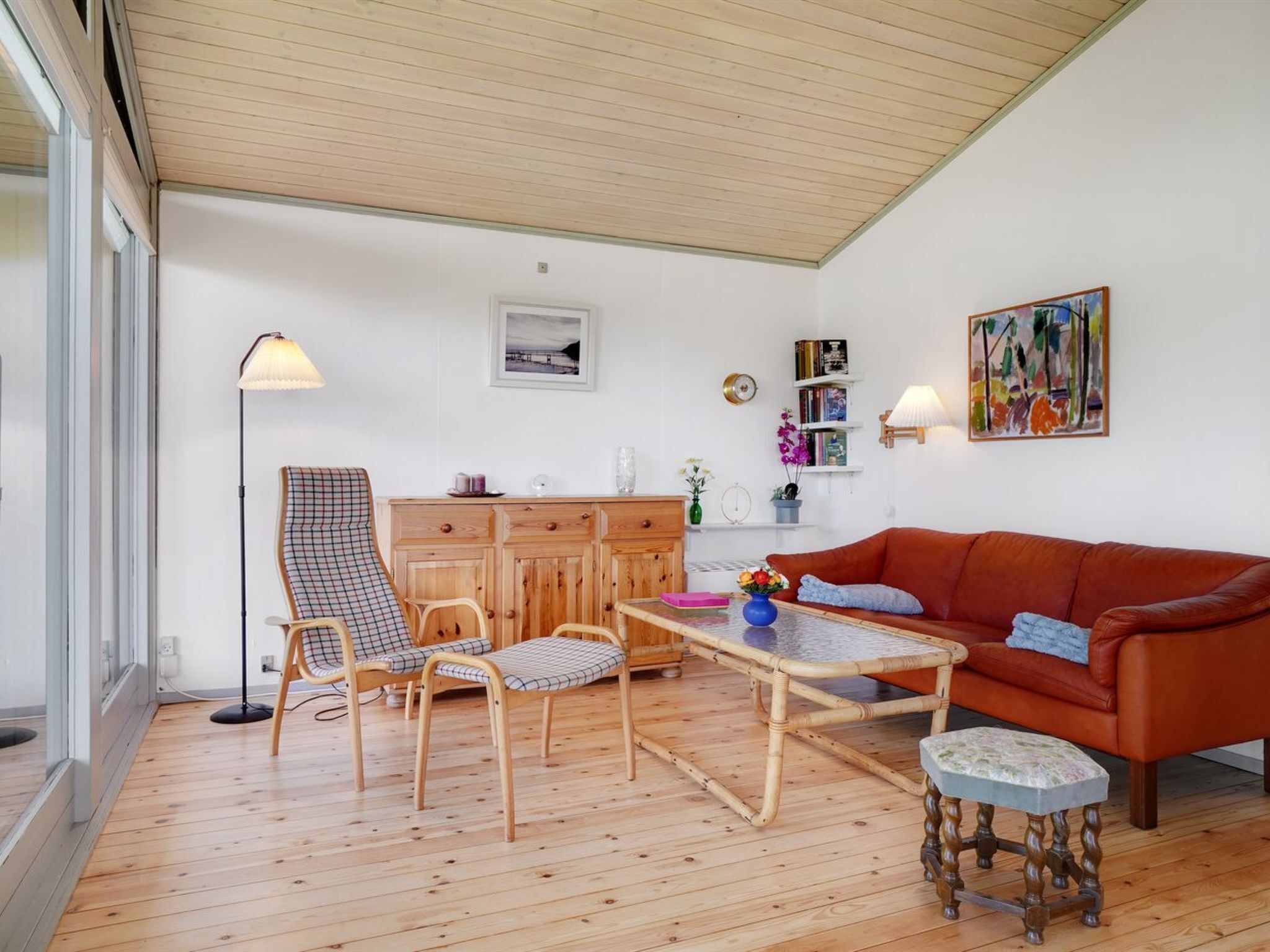 A cozy living room with a wooden floor, a red sofa, a patterned armchair, a coffee table, and a floor lamp.