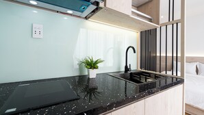 A modern kitchen with a black countertop, a sink, a plant, and a tablet. - Haya Bac Hai Apartments (Ho Chi Minh City)