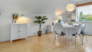 A dining area with a white table, chairs, a potted plant, and a pendant light.