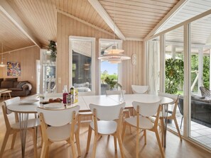 Un espace de repas moderne, doté d’une grande table et de chaises, d’un plancher en bois et de grandes fenêtres offrant une vue sur l’extérieur.