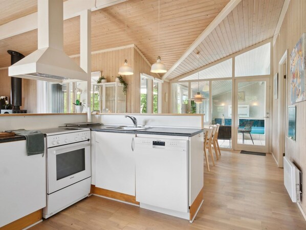 Une cuisine moderne avec des meubles blancs, un four encastré et un lave-vaisselle. Une grande fenêtre offre une lumière naturelle et une vue sur l’extérieur.