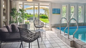Et indendørs poolområde med pool, liggestole og en ventilator.