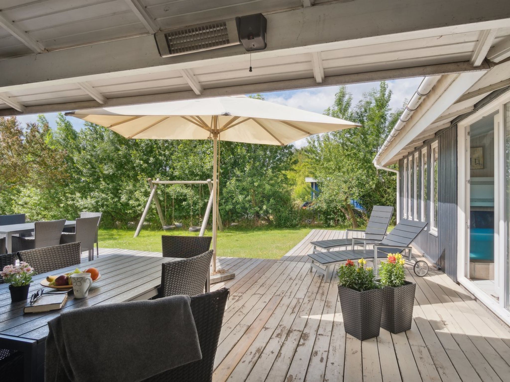 A covered outdoor patio with a swing set, dining table, and lounge chairs.