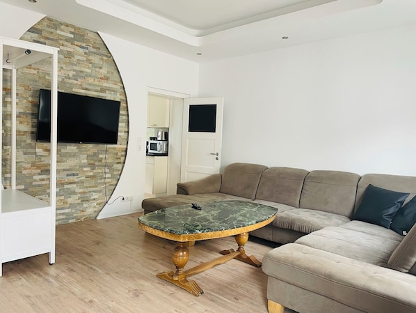 Una sala de estar moderna con una pared de piedra, una mesa redonda con cubierta de mármol, un sofá color beige y un televisor montado en la pared.