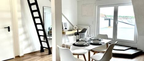 Un comedor con una mesa dispuesta para cuatro, una escalera en la esquina y vistas del exterior a través de un ventanal grande.