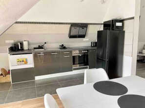 A modern kitchen with a built-in oven, a black refrigerator, and a white dining table with black circular accents. - MyStay: *Travel & Business* (Nußloch)