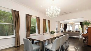 A spacious dining area with a long table, grey upholstered chairs, and a chandelier. - Inner City Resort  (St Kilda)