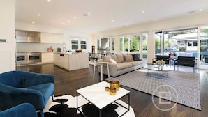 A modern open-plan living area with a kitchen, a dining area, and a seating space with a view. - Inner City Resort  (St Kilda)