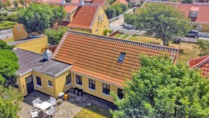 Ein Wohngebiet mit Häusern und roten Ziegeldächern, ein gelbes Haus mit Terrasse und im Hintergrund der Blick auf das Meer.
