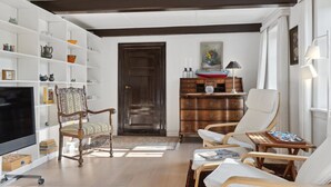 Ein Wohnzimmer mit Fernseher, Holzstühlen, Bücherregal und Kommode.