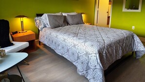 Ein Schlafzimmer mit einem Bett, einem Nachttisch, einer Lampe und einer Wand mit Kunstwerken.