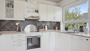 A modern kitchen with white cabinets, a built-in oven, and a window providing a view of the outdoors.