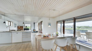 Een moderne keuken met een centraal eiland, houten vloeren en grote ramen met uitzicht op de omgeving.