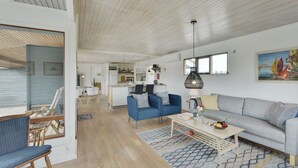 Een ruime woonkamer met houten plafond, een eethoek en een keuken op de achtergrond.