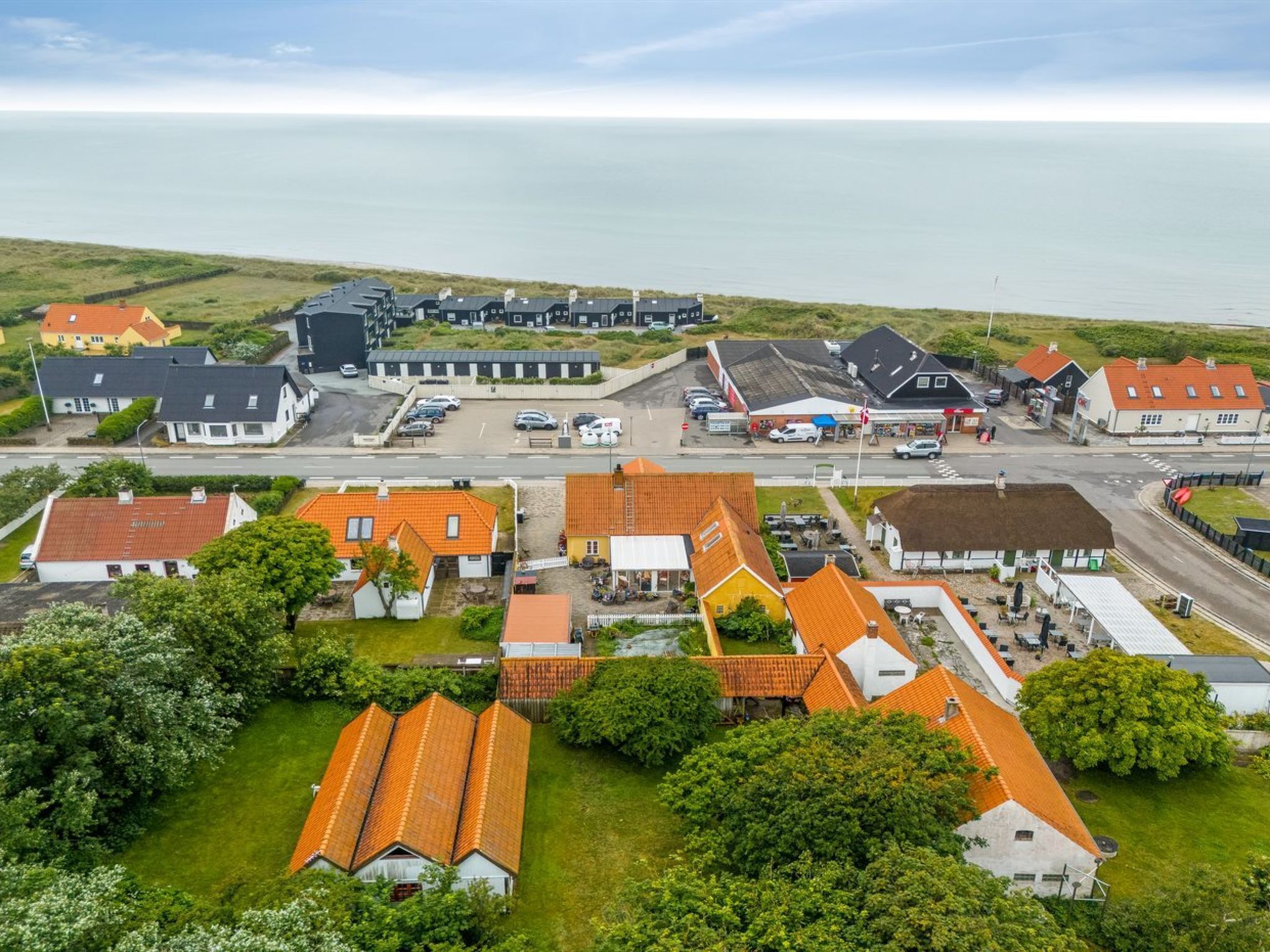 An aerial view of a coastal village with houses, a small commercial area, and a road leading to the sea.