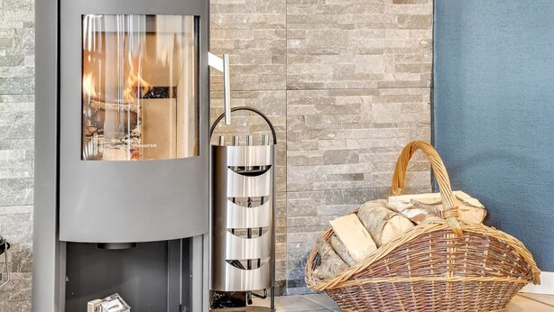 Una chimenea moderna con recinto de vidrio, un soporte metálico para leña y una cesta de mimbre.