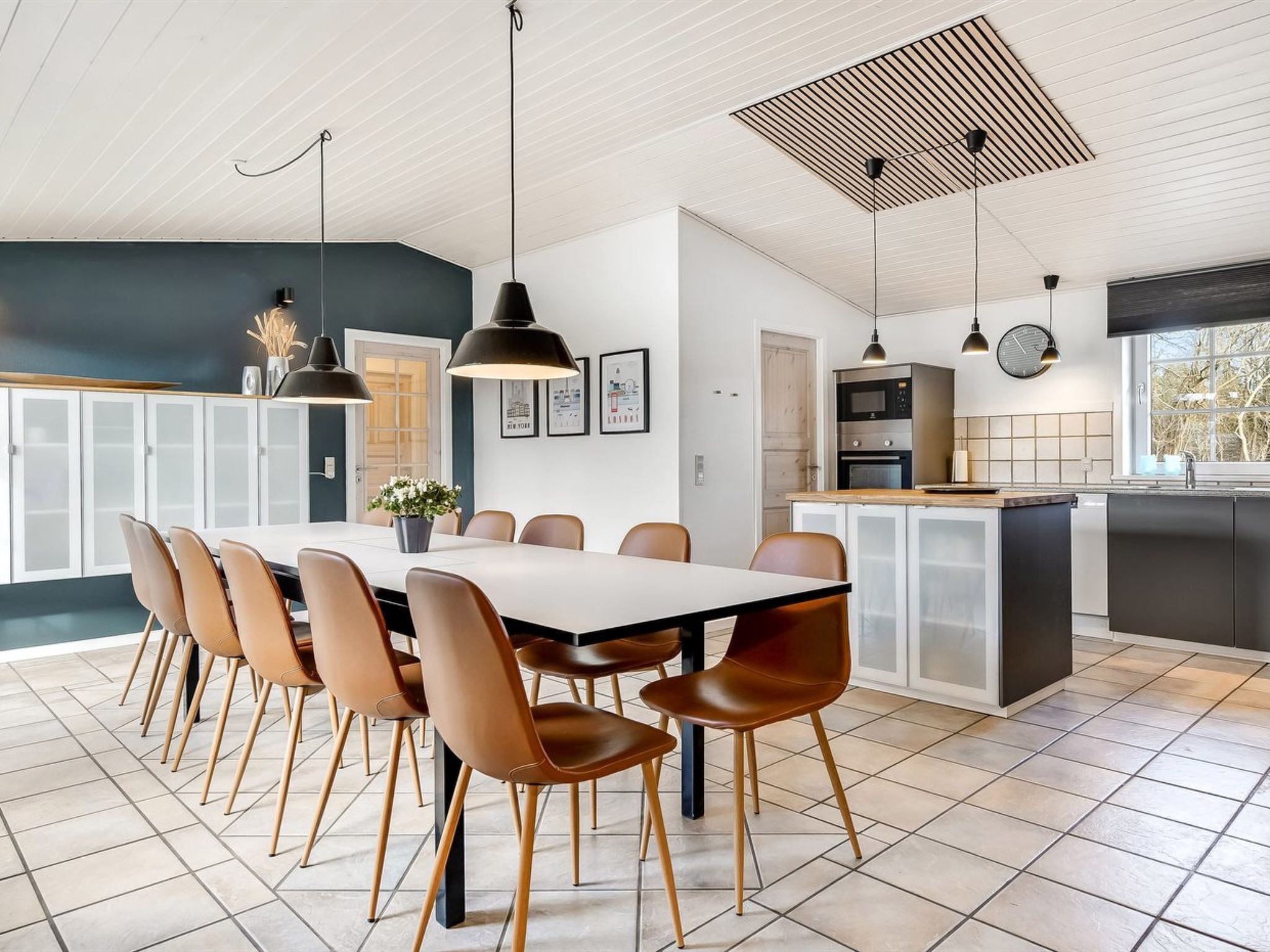 A modern kitchen with a central island, a dining area with a long table and chairs, and pendant lighting.