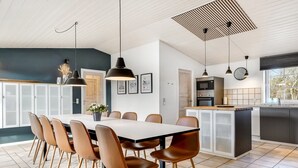 Una cocina moderna con una isla central, un comedor con una mesa larga y sillas, e iluminación colgante.