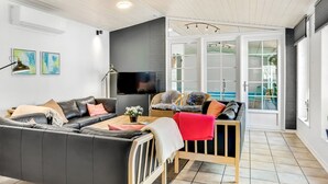 Una sala de estar moderna con un sofá de cuero negro, una mesa de centro de madera y una televisión. Hay un balcón con vista al mar.