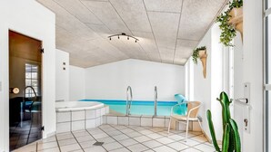 Un baño moderno con una bañera grande, ducha y una pequeña zona de estar con una silla y una planta en maceta.