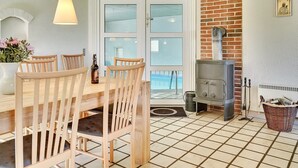Een knus vertrek met een houten tafel en stoelen, een bakstenen muur, een fornuis en een raam met gezandstraald glas.