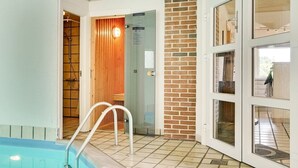 Een zwembad met betegelde vloer en een houten deur naar een sauna.