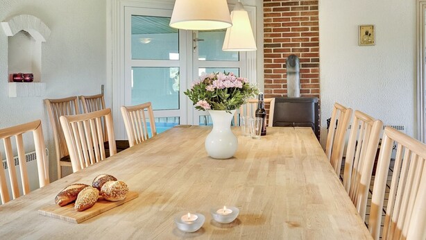 Een eetgedeelte met een houten tafel, stoelen, een bloemenvaas en een broodmand.