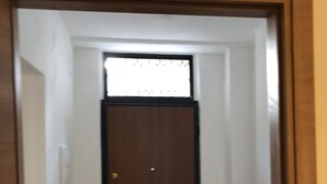 Un couloir étroit avec une porte en bois, une petite armoire blanche et une fenêtre au fond.