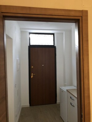 Un pasillo estrecho con una puerta de madera, un armario pequeño blanco y una ventana al final.