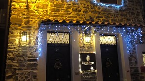 Un bâtiment en pierre avec deux portes sombres, chacune portant un numéro. Le bâtiment est décoré de guirlandes lumineuses bleues et affiche une enseigne sur laquelle on peut lire « Ca’delBorgo ».