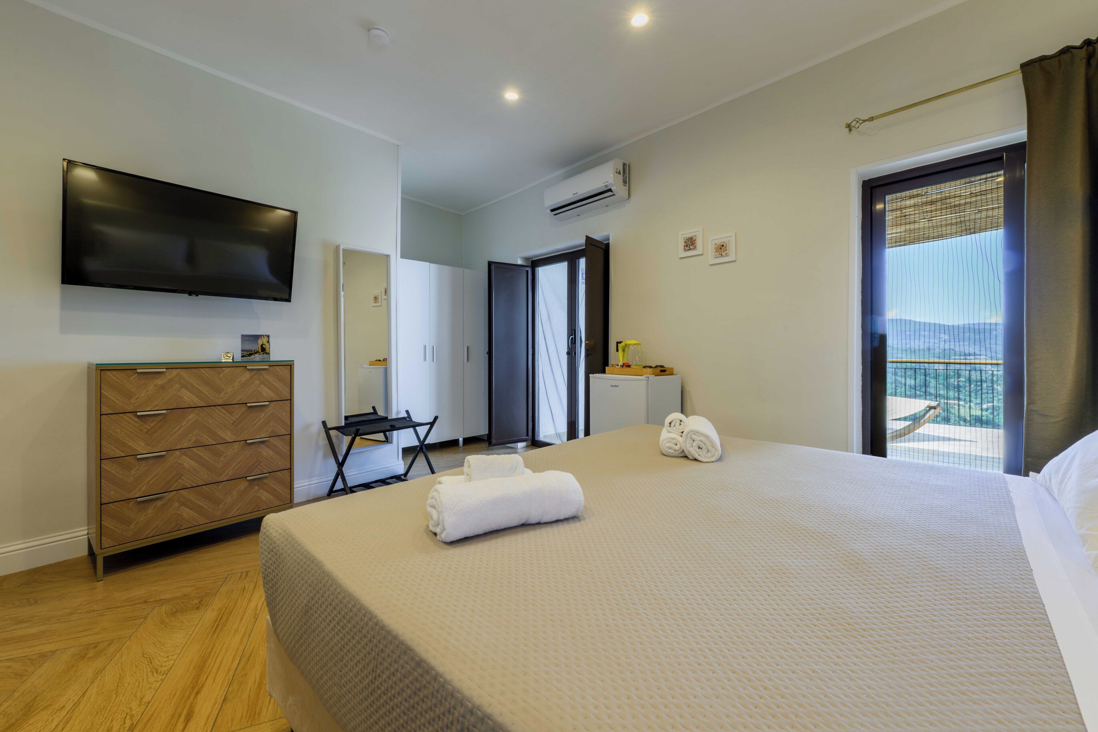 A hotel room with a bed, a desk, a dresser, a television, and a balcony with a view.