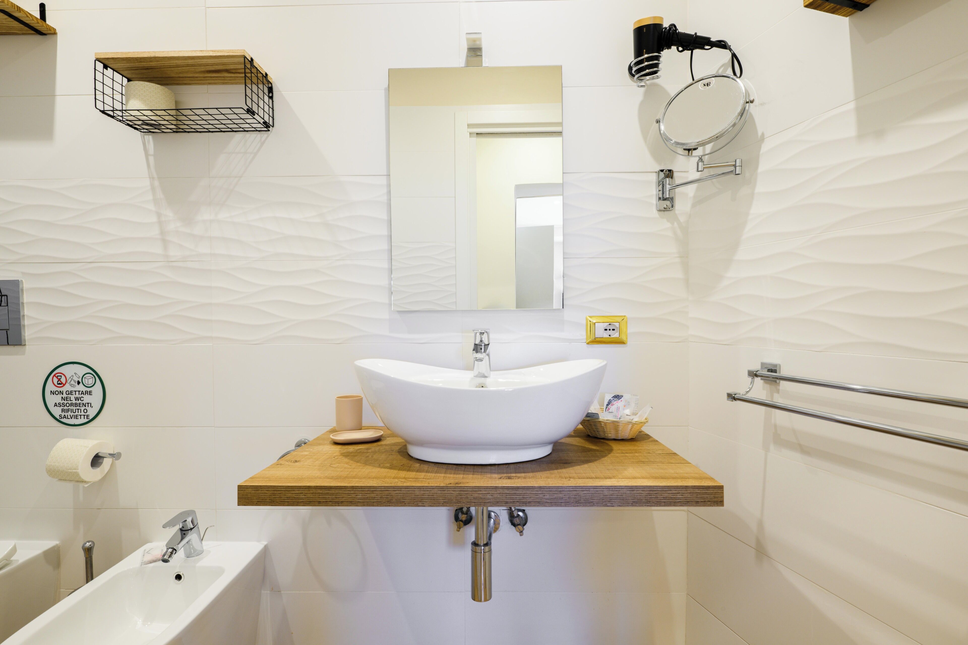 Un baño con lavamanos independiente, un espejo, toallero y dispensador de papel higiénico.