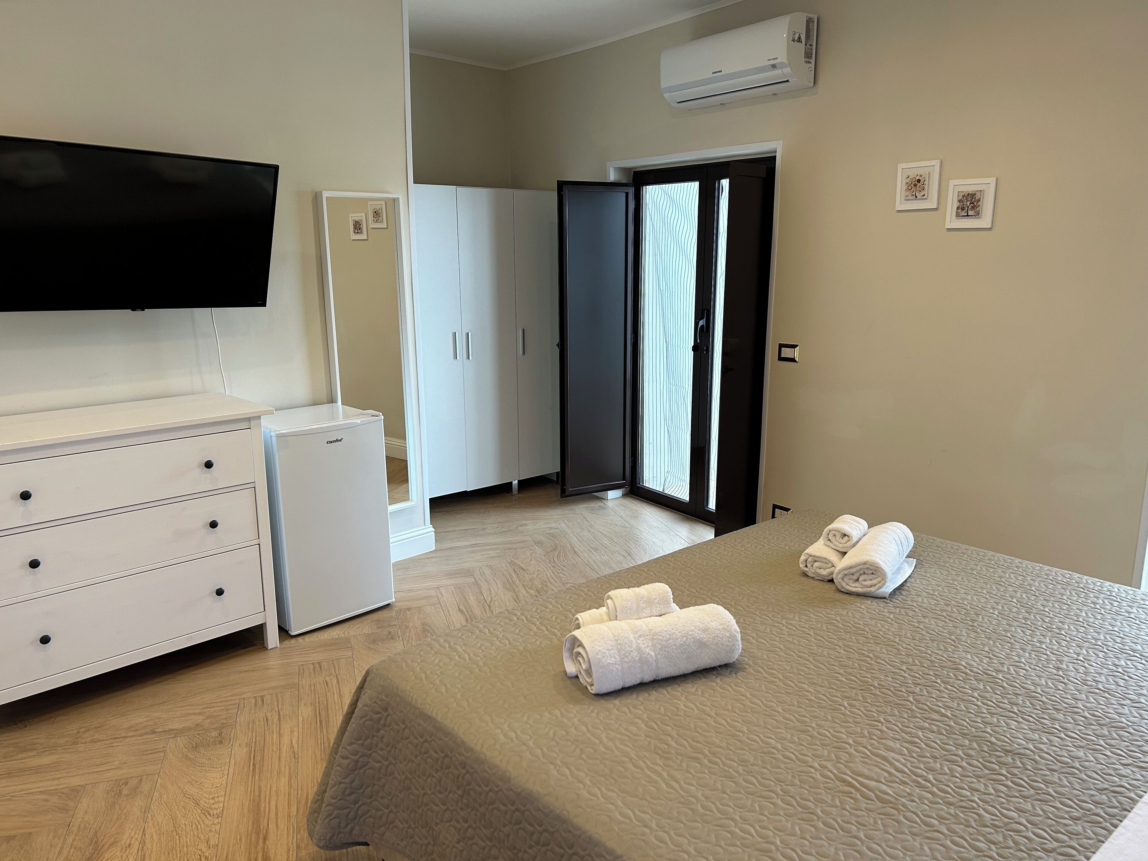 Une chambre d’hôtel équipée d’un lit, d’une télévision, d’un mini-bar, d’une armoire et d’une porte coulissante donnant sur un balcon.