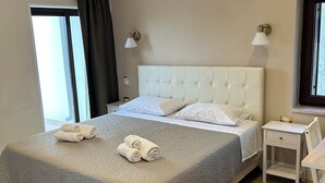 Un lit bien fait, recouvert d’une couette grise, deux tables de chevet et une fenêtre avec des rideaux.