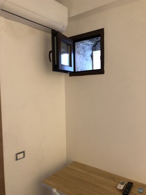 Una habitación con una ventana pequeña, una mesa de madera y un aire acondicionado fijado a la pared.