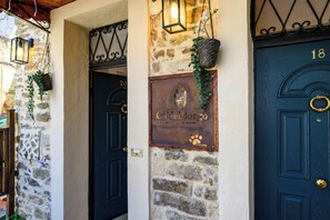 A rustic building with stone walls, a metal gate, and two dark blue doors with numbers 18 and 20.