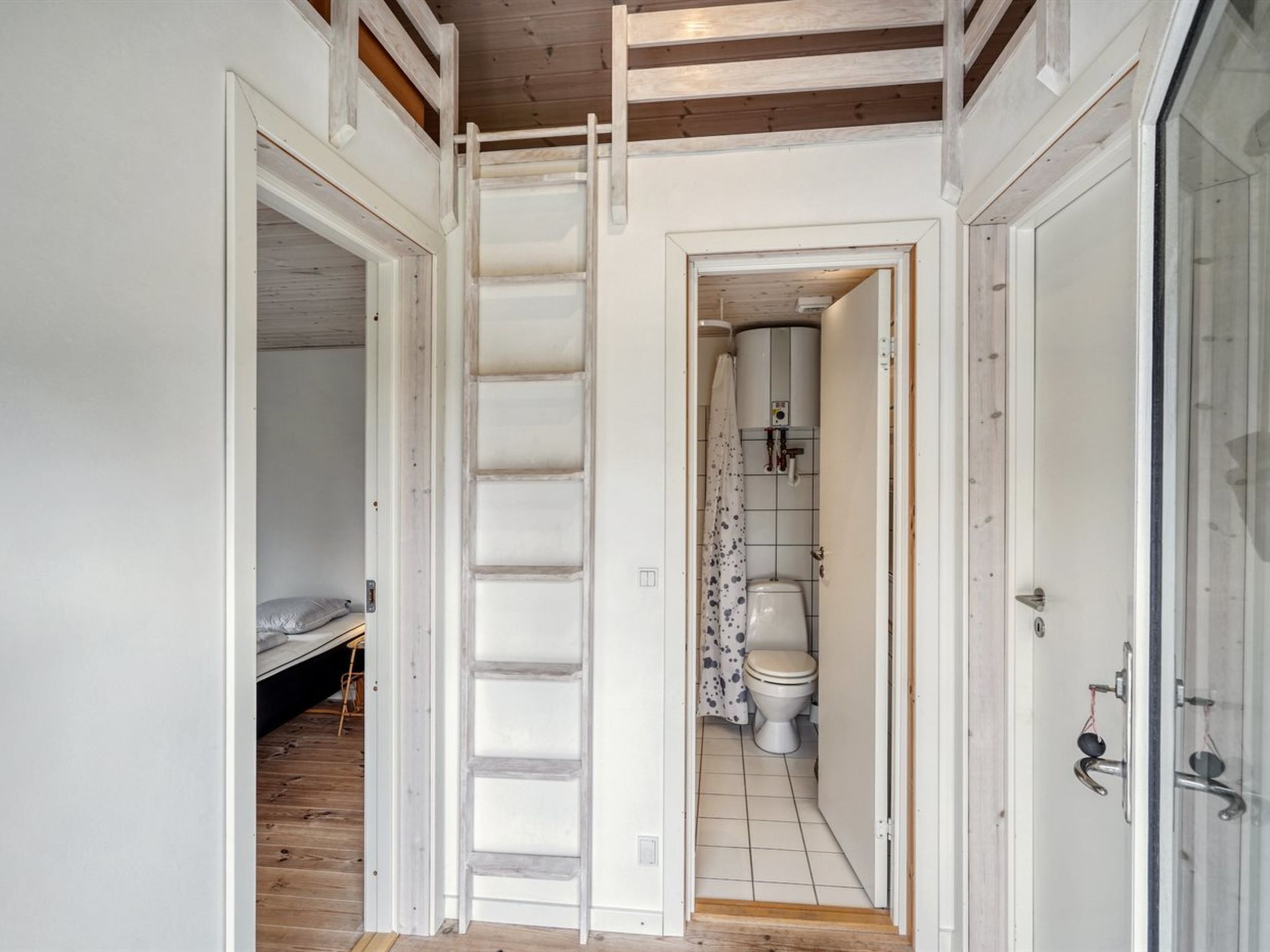 Een kleine kamer met een hoogslaper, een witte deur en een badkamer met toilet en douche.