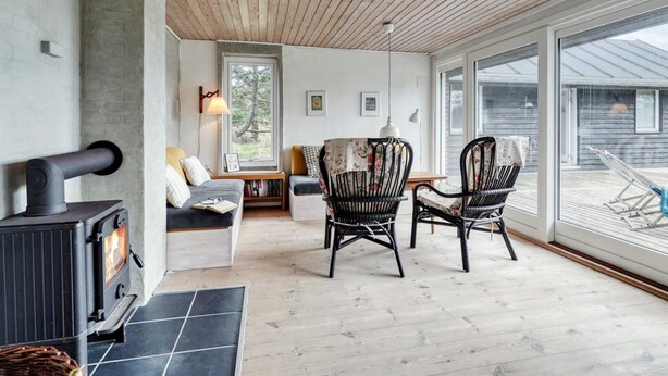 A cozy room with a fireplace, a sofa, two wicker chairs, and a large window offering a view of the outside. - "Thorgisl" - 1.4km from the sea by Interhome (Blåvand)