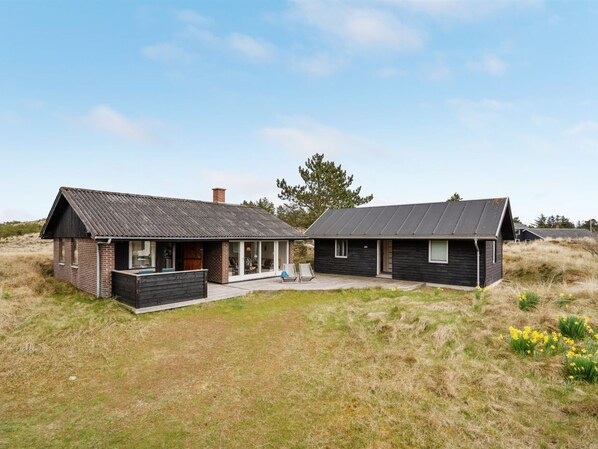 A modern two-story house with a flat roof, large windows, and a patio area.