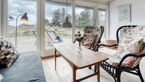 A cozy room with a wooden ceiling, a large window, a wooden table, a floral chair, and a sofa. - "Thorgisl" - 1.4km from the sea by Interhome (Blåvand)