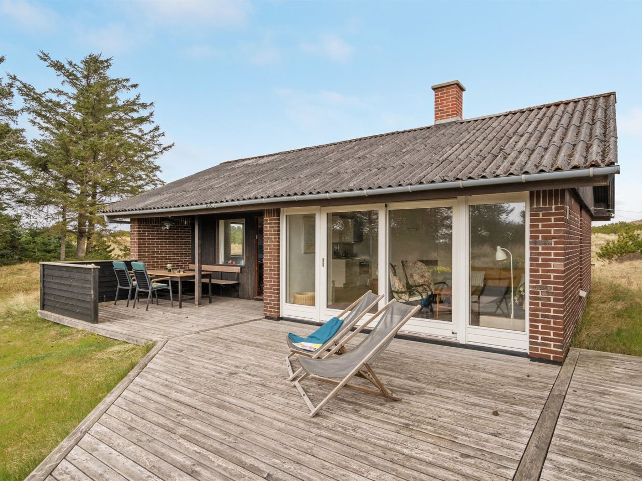 A modern house with a wooden deck, a dining area, and a lounge chair.