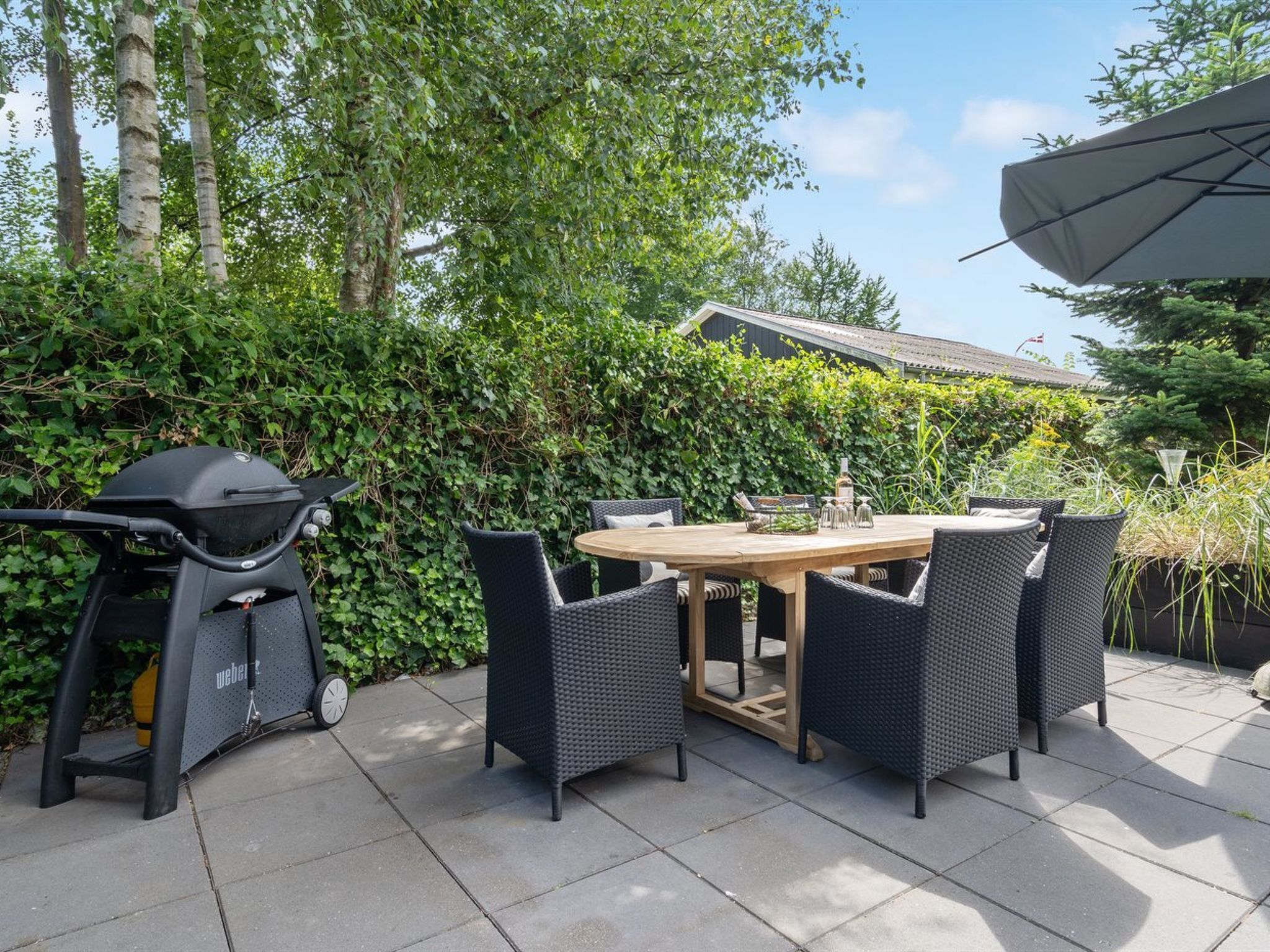 An outdoor patio with a round table and four chairs, a grill, and a large umbrella.