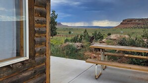 Una cabaña de troncos con un ventanal grande y una mesa de picnic en un patio de concreto.