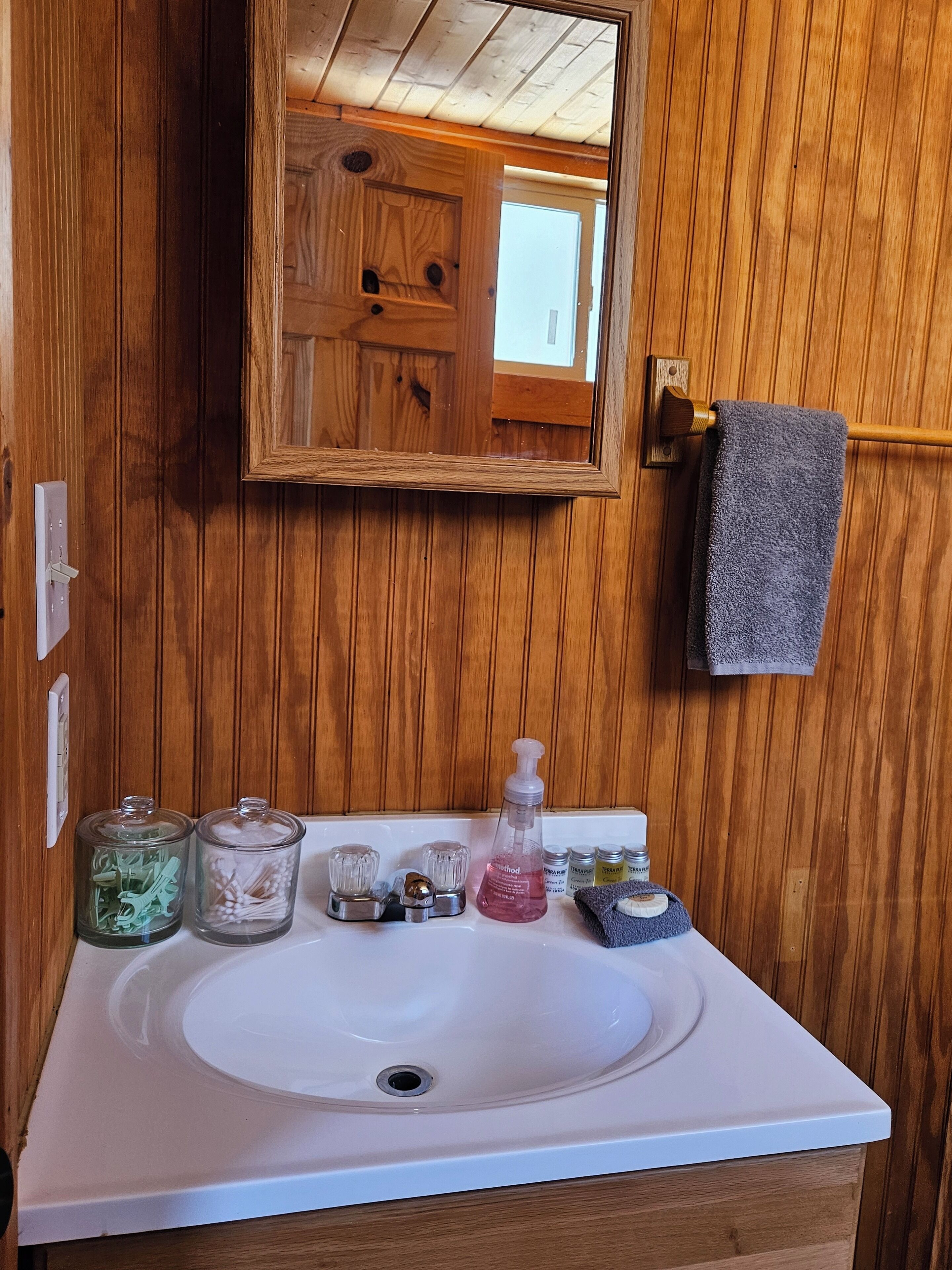 Ein Badezimmer mit einer Holzwand, einem weißen Waschbecken und einem Spiegel.
