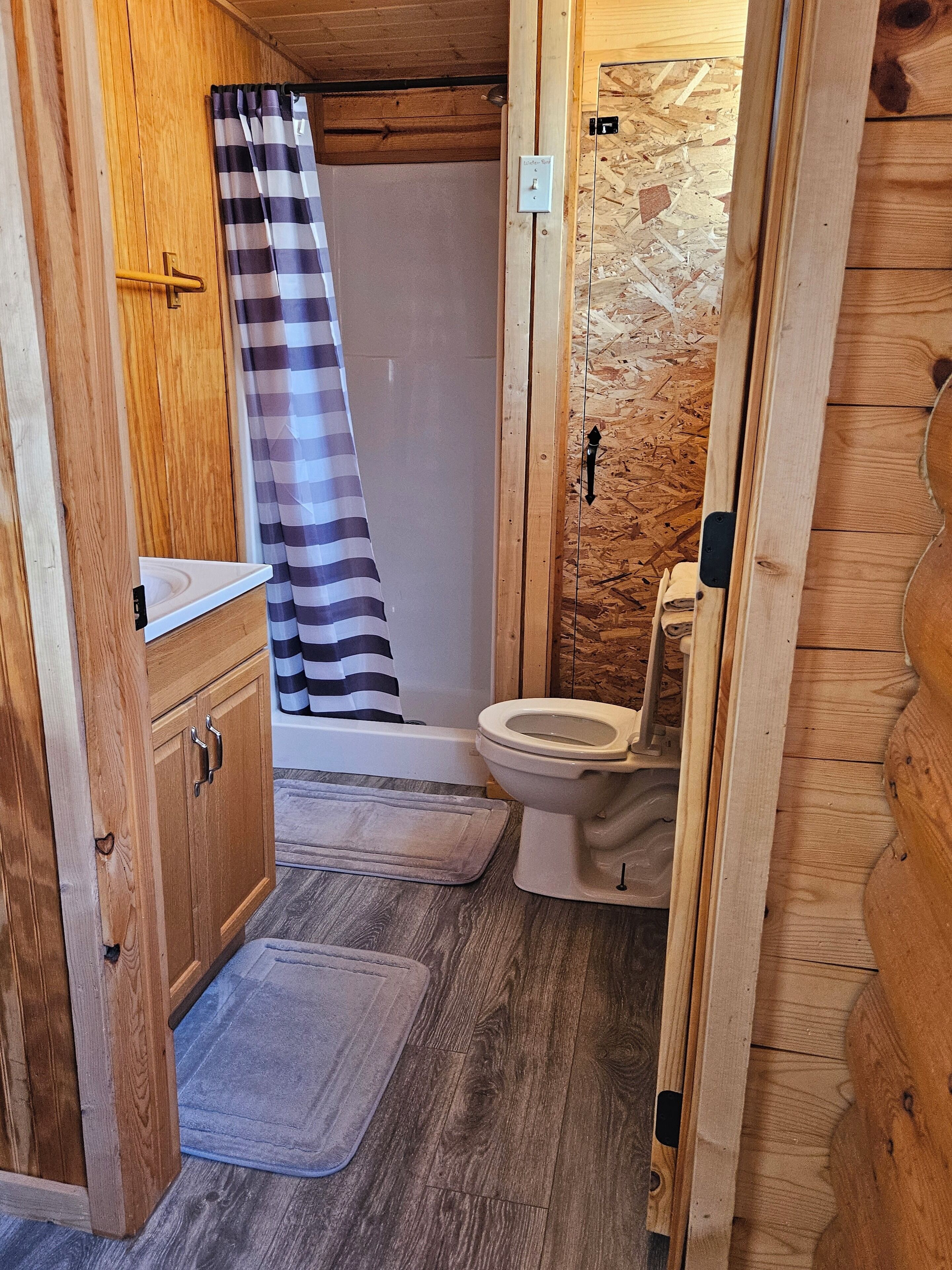 Ein kleines Badezimmer aus Holz mit Dusche, Toilette und einem Hängeschrank.