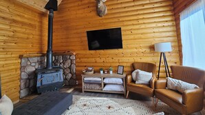 Interior acogedor de una cabaña con chimenea de piedra, cabeza de venado montada, sofá y televisor.
