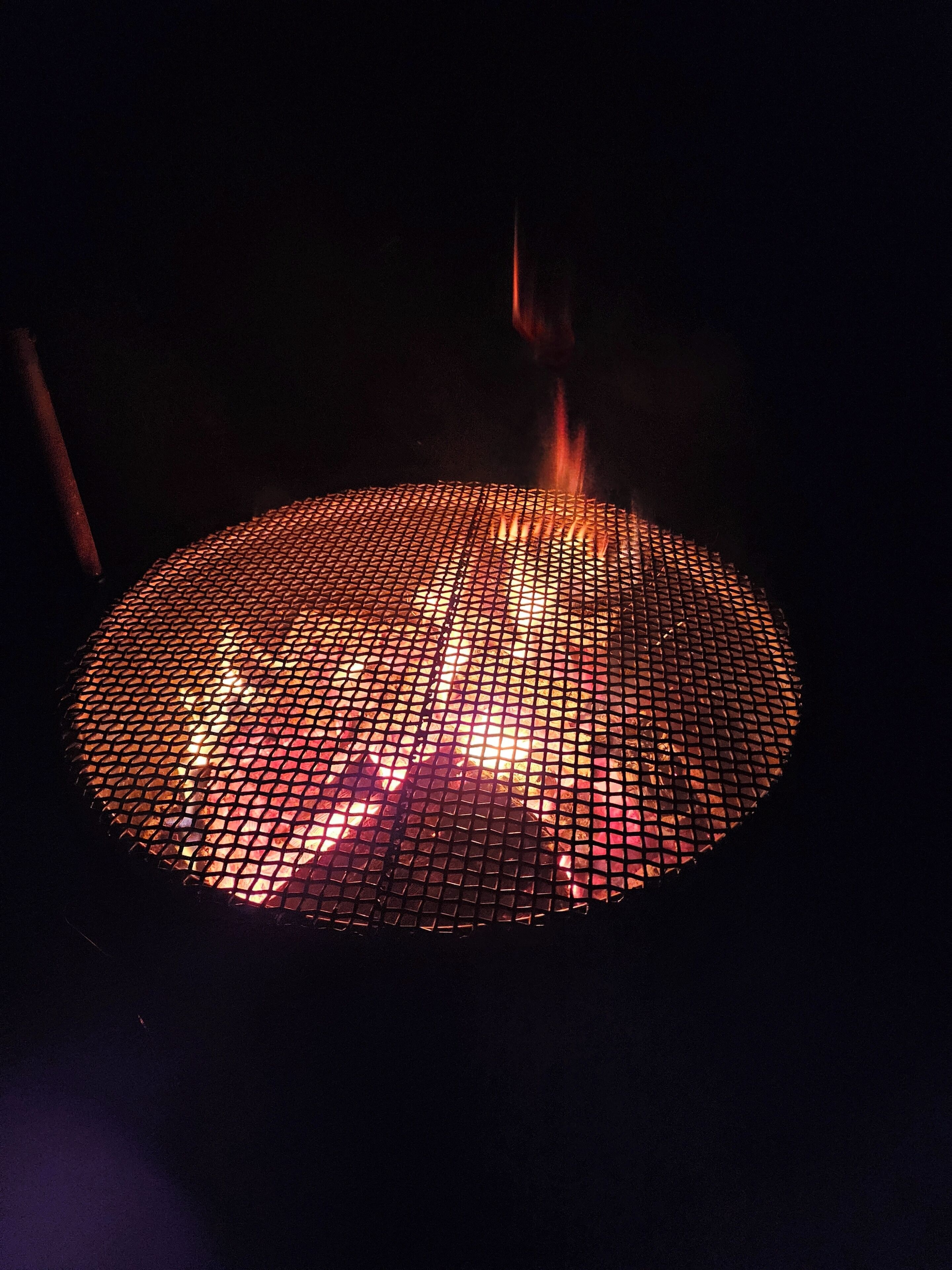 A circular fire pit with a metal grate, surrounded by dark surroundings.