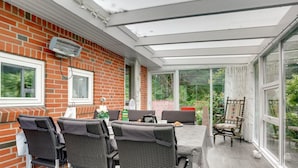 Une véranda avec un mur en briques, de grandes fenêtres et une table entourée de chaises.